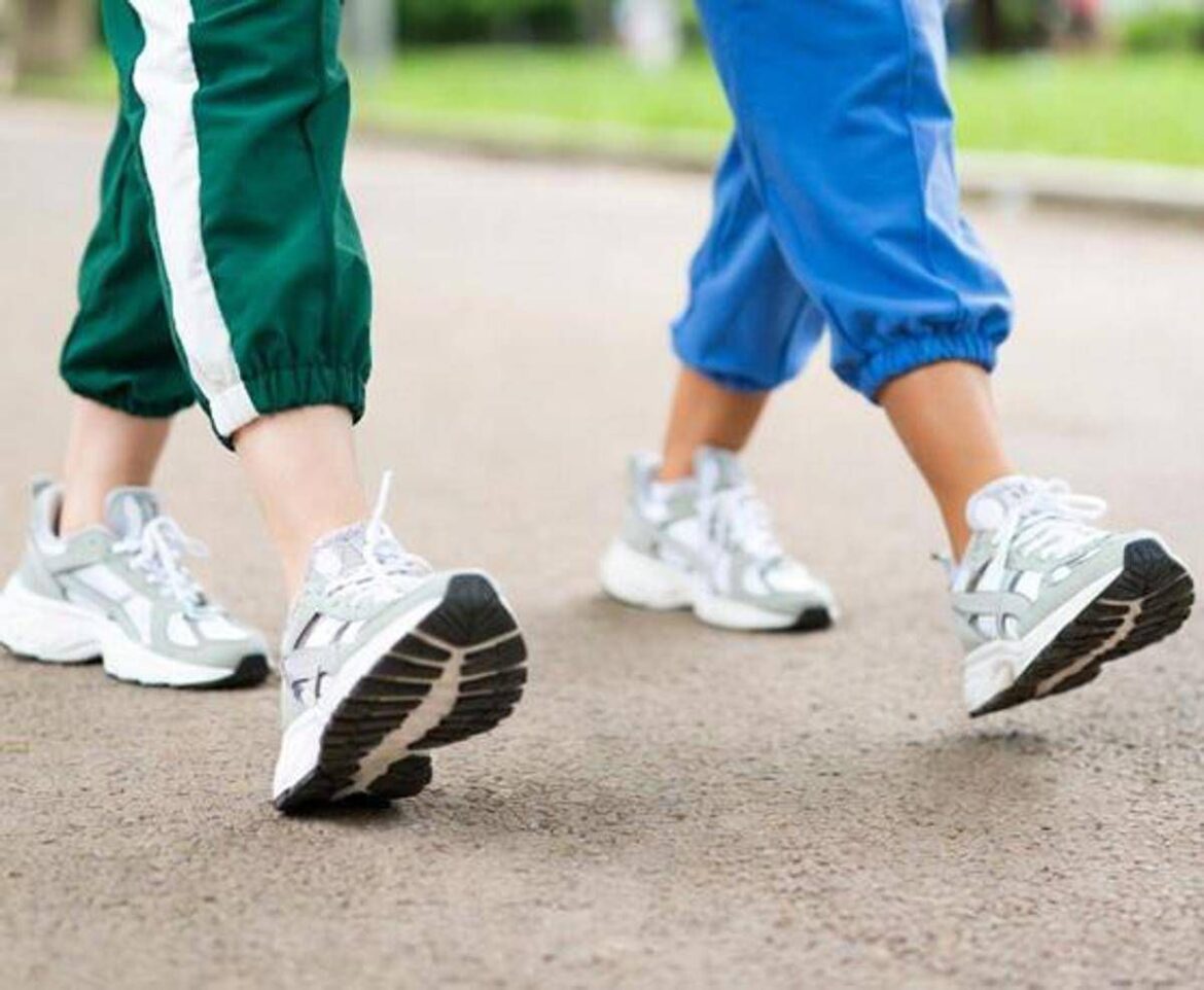 Two people wearing sneakers walk on a paved path, green and blue track pants visible.