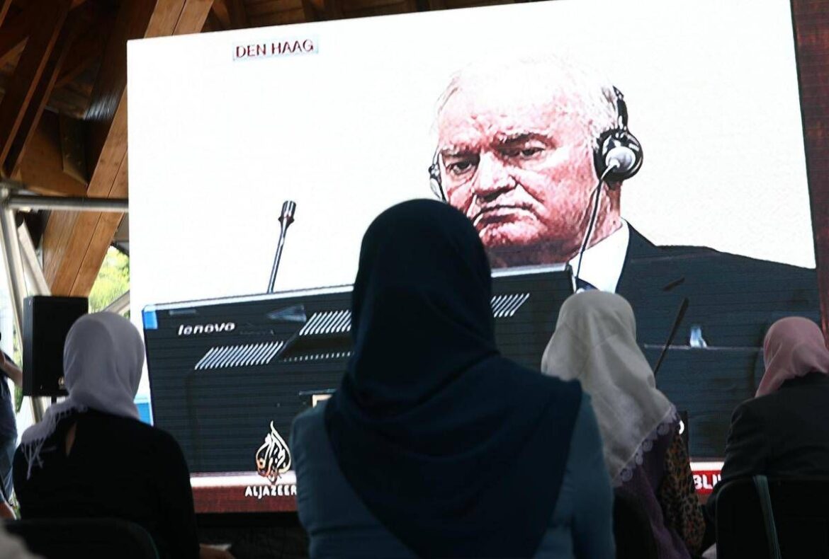 Audience wearing hijabs watches a large screen showing a man with a headset speaking at an event; Den Haag label at top, Al Jazeera logo bottom left/right.